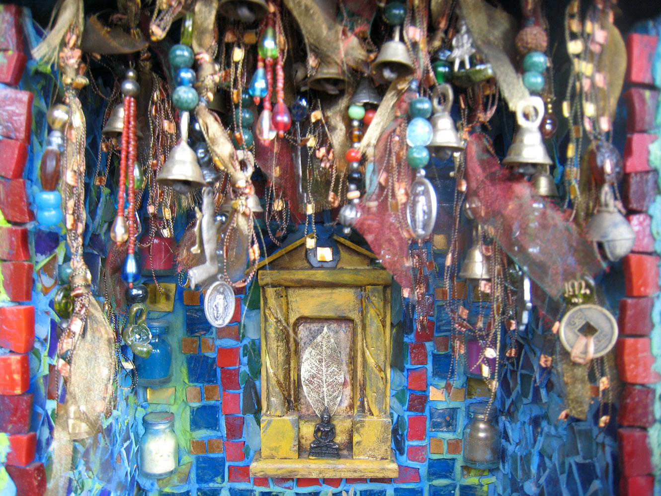 Close-up of reliquary shrine with bells, beads, and mosaic tiles