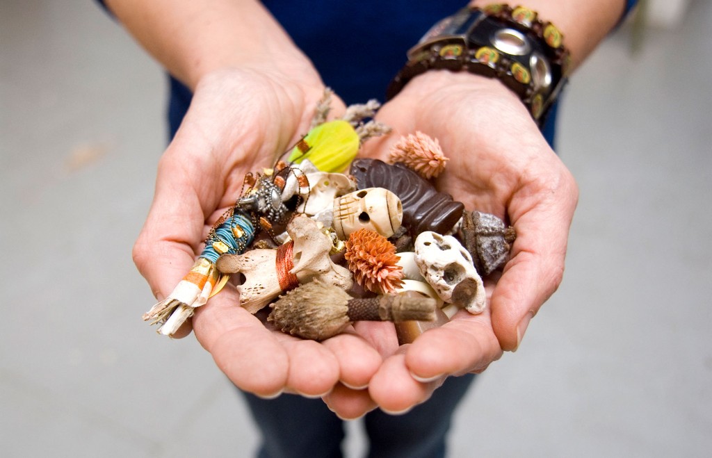 Cupped hands holding a collection of natural and crafted objects—bones, seed pods, feathers, and small treasures